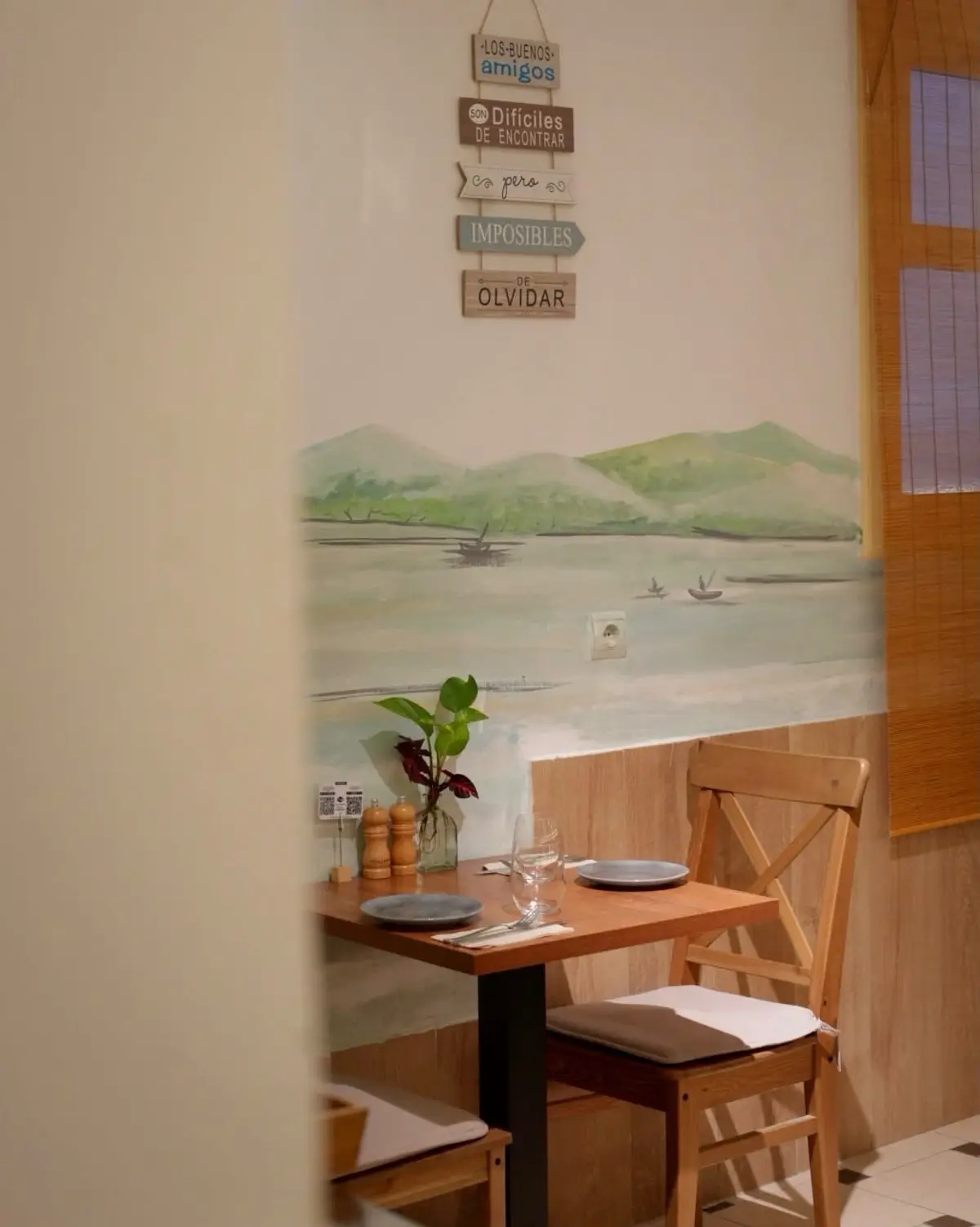 Una mesa para dos bajo un lago pintado, con el cartel «Los buenos amigos son difíciles de encontrar, pero imposibles de olvidar»