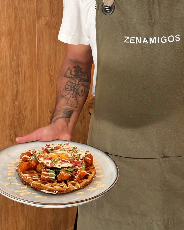 A cook in a ZENAMIGOS apron holding the karaage and waffle with a fried egg