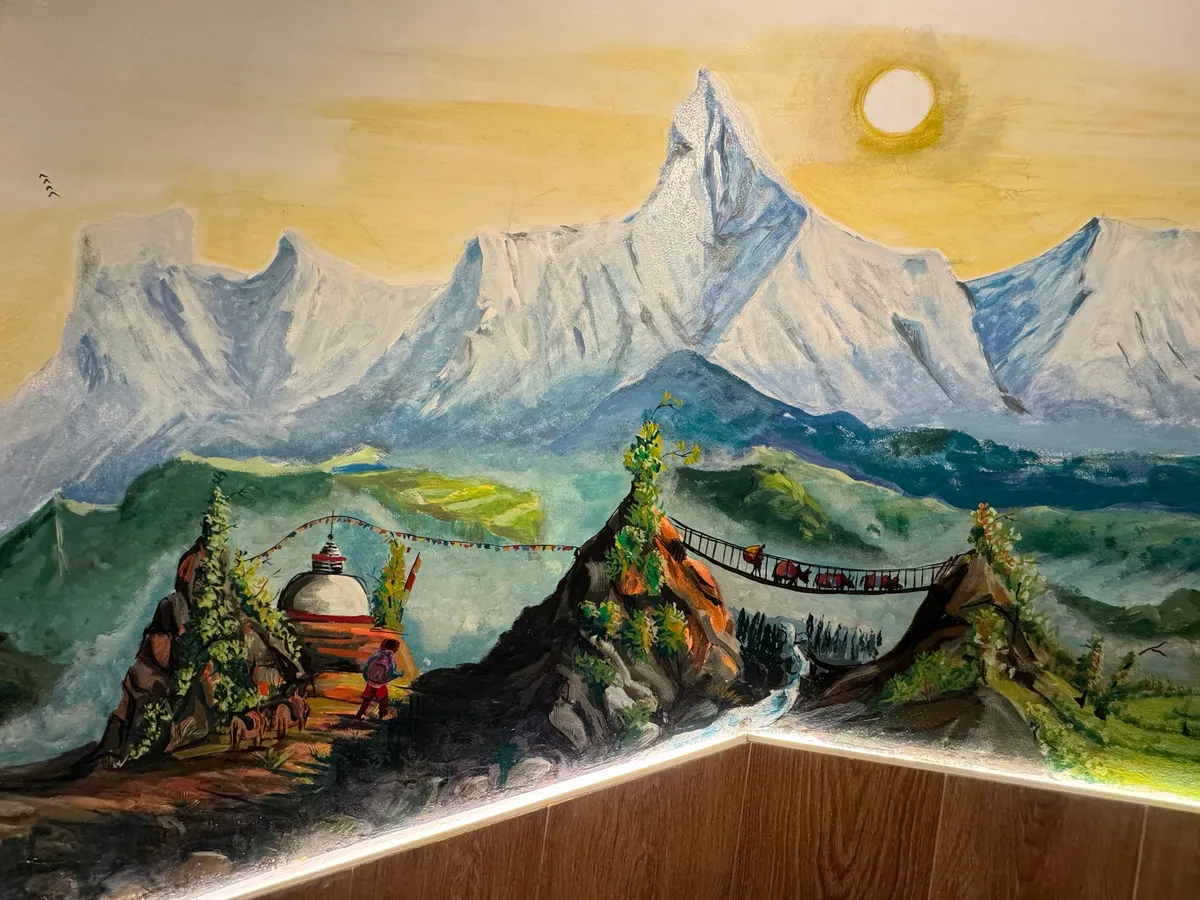 Our wall painting of the Himalayas: snowy peaks, a stupa with prayer flags, a porter on the path and a rope bridge