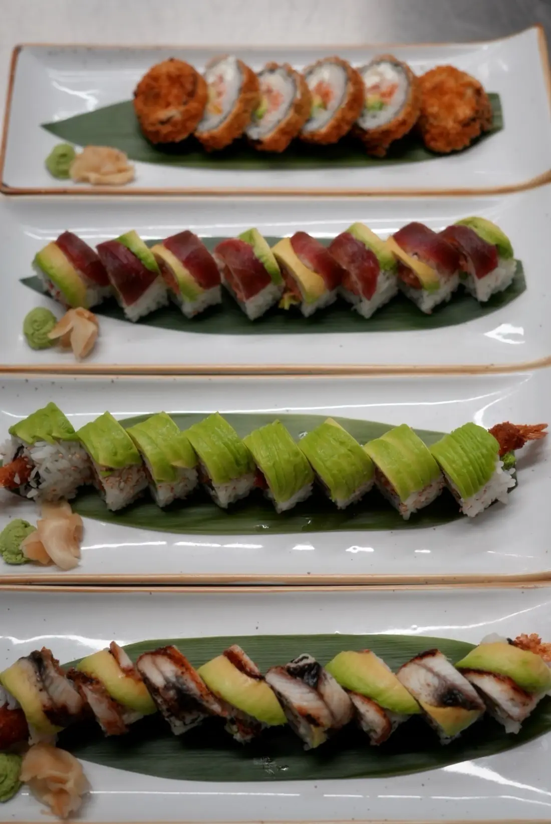 Cuatro platos de rolls de sushi alineados en el pase de nuestra cocina
