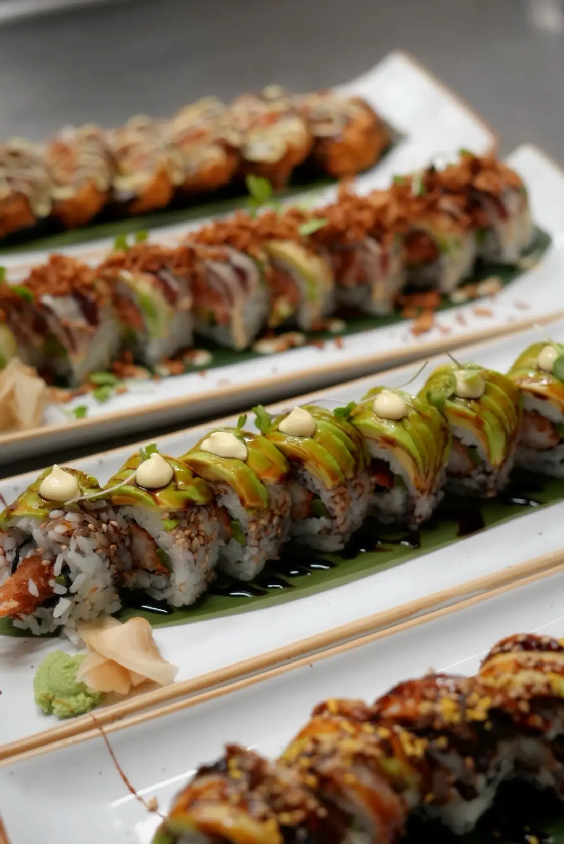 Rolls de sushi coberts d'alvocat, en plats llargs blancs